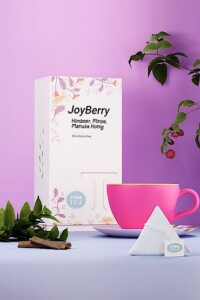Tee mit Verpackung und Tasse auf fliederfarbenem Untergrund